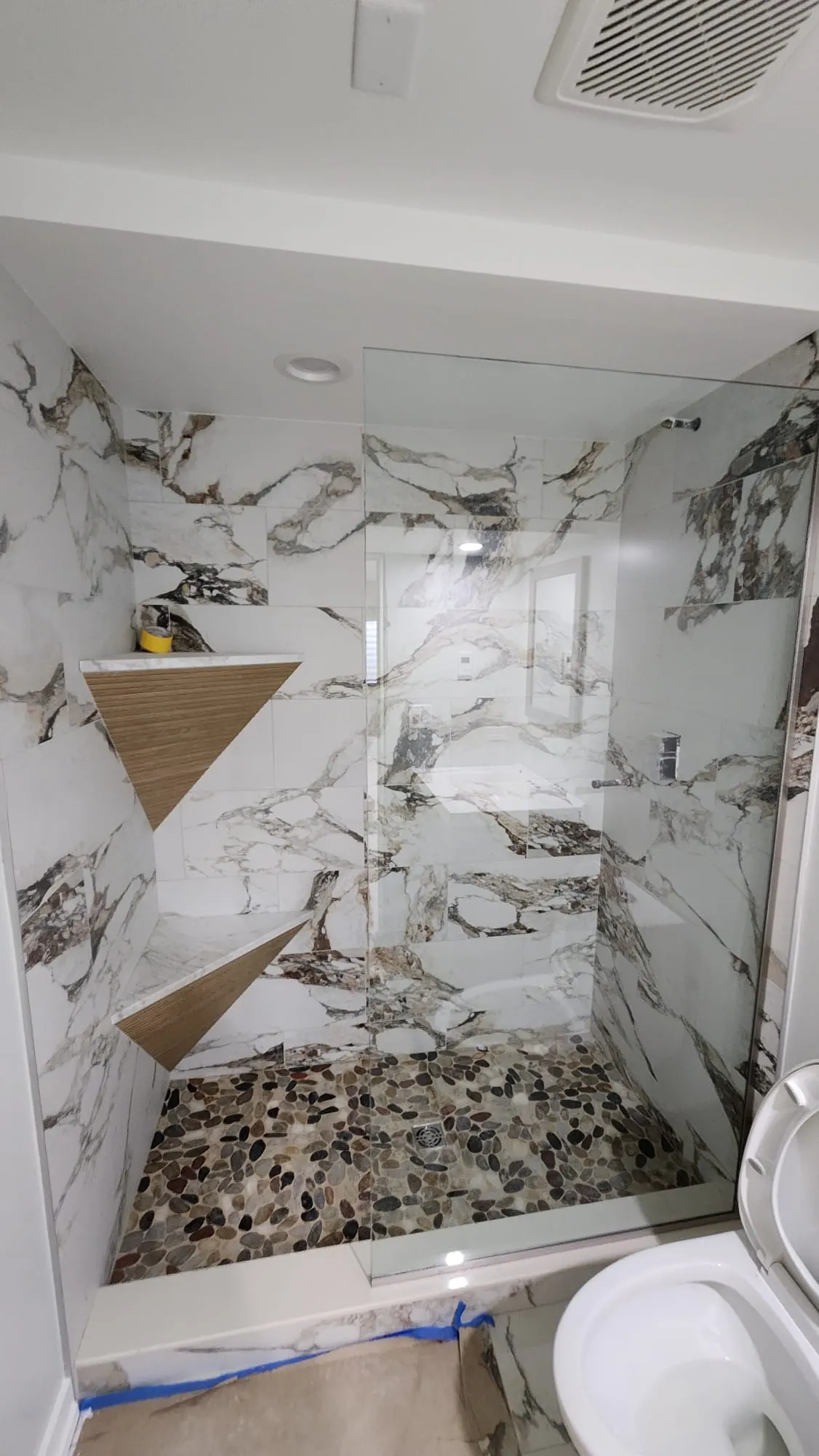 Bathroom remodel with marble-look tile shower, corner shelves, and pebble shower floor in Bloomingdale