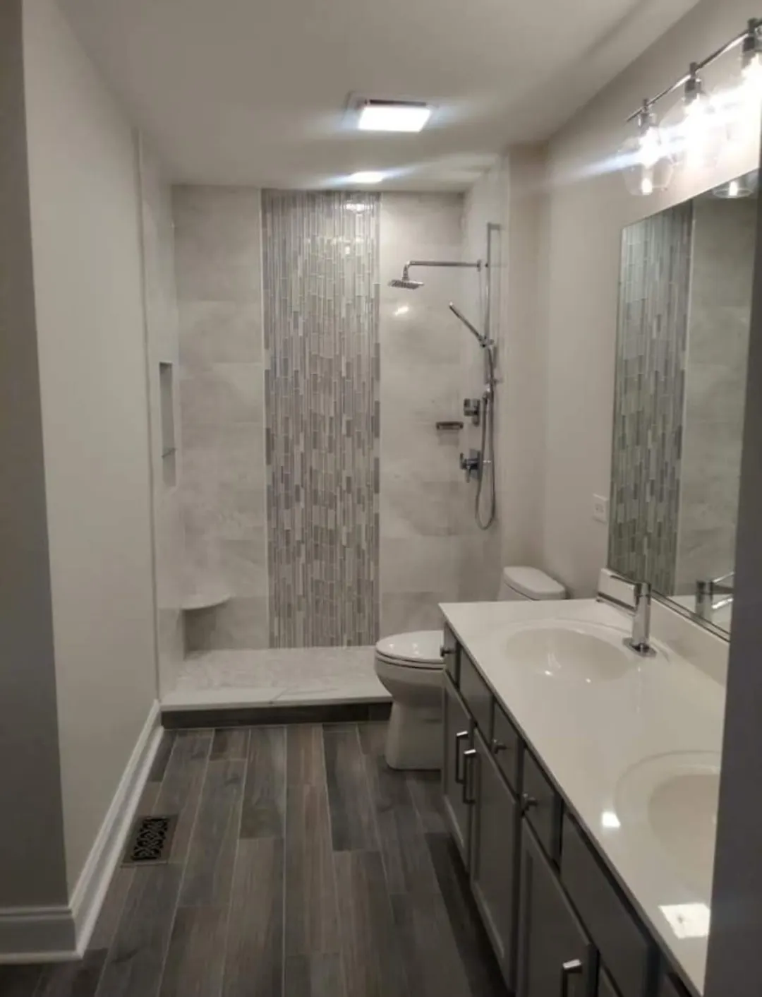 Bathroom remodel with tiled walk-in shower, glass accent strip, and double vanity in Bloomingdale