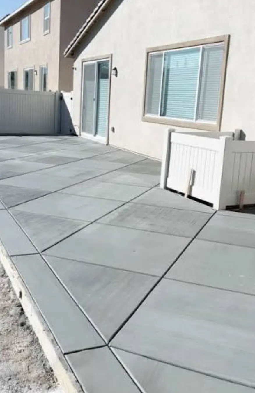 Newly poured concrete patio slab with clean control joints beside a house