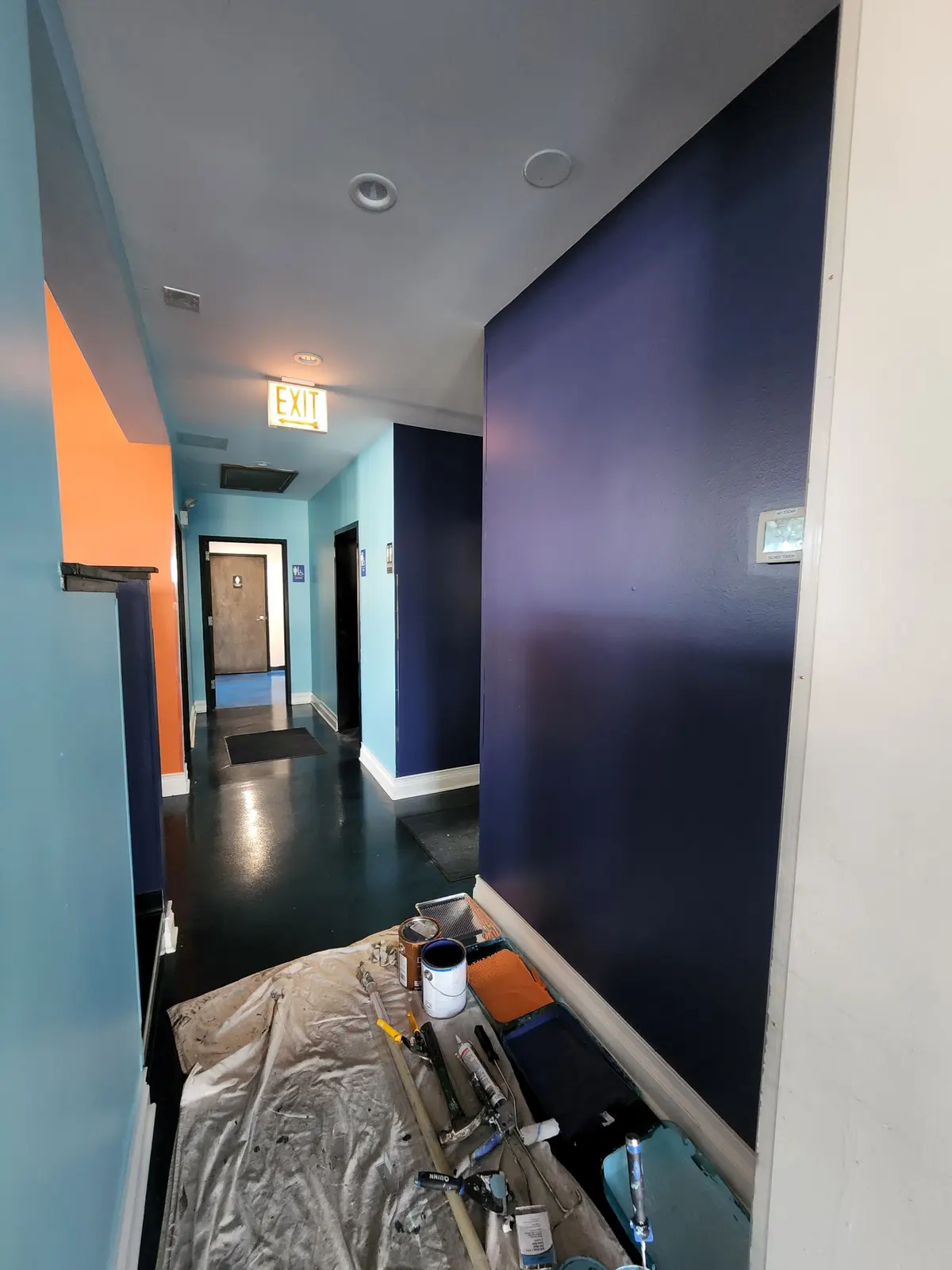 Navy accent wall in a hallway being painted, with drop cloths down